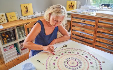 Tina Altus sitzt an einem Tisch und fertigt ein Bild mit Blüten an.