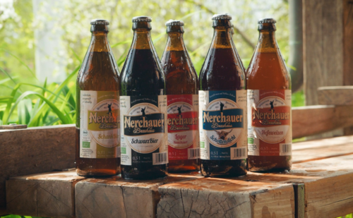 Fünf Biersorten in Flaschen auf einer Holzbank.